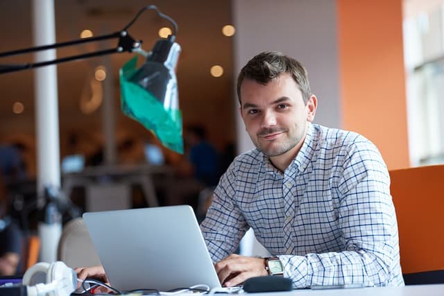 Male cybersecurity student with laptop smiling.
